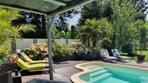 Piscina com espreguiçadeiras e mesa, cercada por um jardim com diversas plantas e flores.
