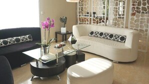 Uma sala de estar moderna com sofá branco, almofadas estampadas em preto e branco, mesa de centro de vidro e uma parede decorativa com padrão que imita pedra.