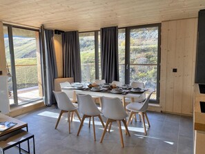 A dining area with a large table, white chairs, and a view of a mountainous landscape through large windows.