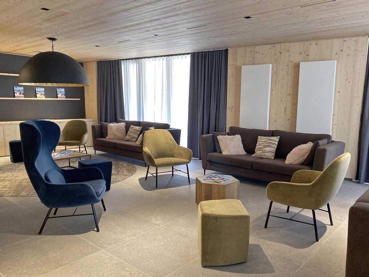 A modern living room with a blue armchair, a yellow armchair, a brown sofa, and a wooden coffee table.