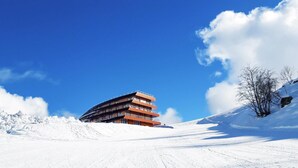 Un hotel de varios pisos con un diseño arquitectónico moderno, ubicado en una ladera nevada.