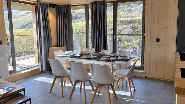 Comedor con una mesa grande dispuesta para seis personas, rodeada de sillas blancas con patas de madera.