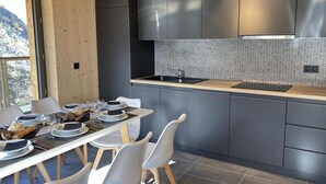 Una cocina moderna con armarios grises, salpicadero de azulejos y un comedor con sillas blancas y una mesa para cuatro.