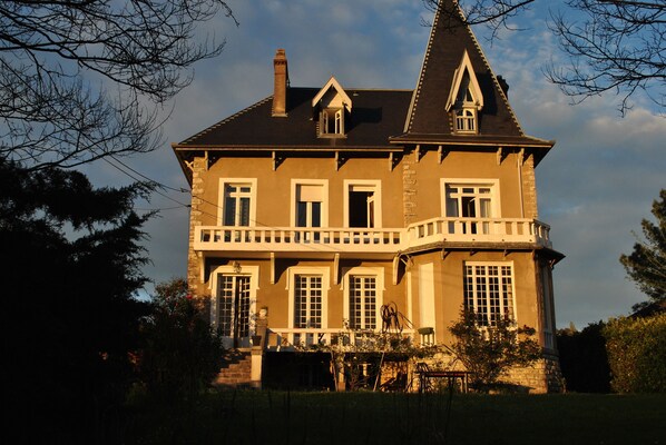 A large, two-story house with a prominent tower, multiple windows, and a balcony.
