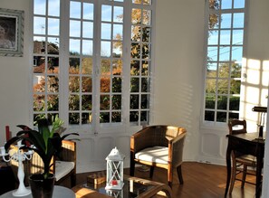 A room with large windows, wicker furniture, and a potted plant.