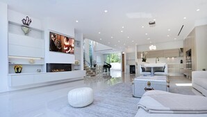 A modern living room with a flat-screen TV, a piano, a dining area, and a kitchen.