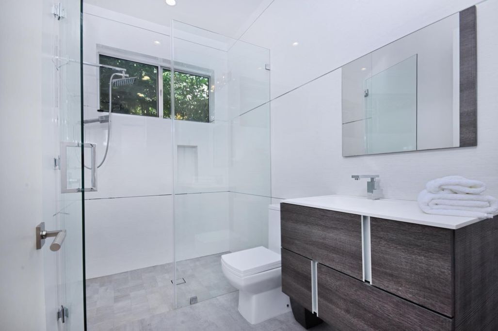 A modern bathroom with a glass shower enclosure, a white toilet, and a vanity with a mirror.