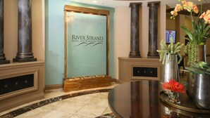 Un espace d’accueil doté d’une porte en verre portant l’inscription « River Strand Golf and Country Club », d’un sol en marbre et d’une table ronde ornée de vases de fleurs.