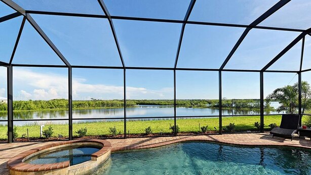 Une piscine avec un jacuzzi, entourée d’une terrasse couverte d’où l’on peut admirer un lac et la verdure environnante.