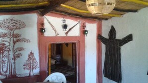 Une pièce dotée d’un toit de chaume, d’une porte à cadre rouge et d’un mur orné d’une fresque représentant un arbre.