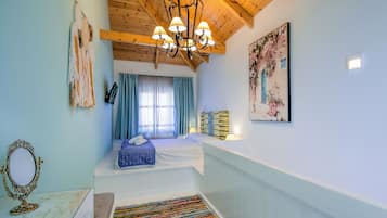 Quarto com cama, lustre, espelho, pintura e janela com cortinas.