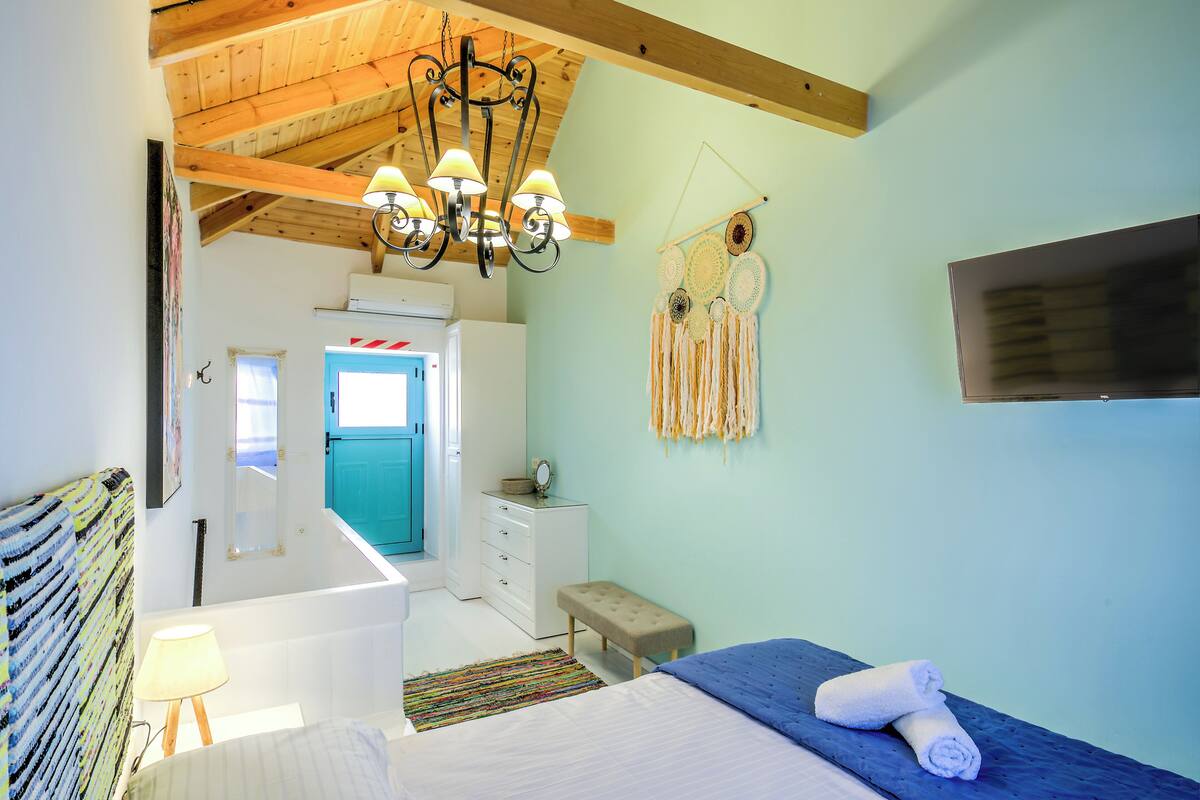 Un dormitorio con cama, banco, cómoda, espejo, candelabro y televisor montado en la pared.