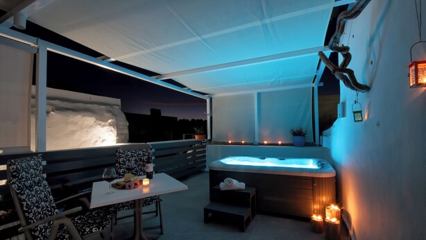 Een modern terras buiten met een jacuzzi, zitplaatsen en sfeerverlichting.