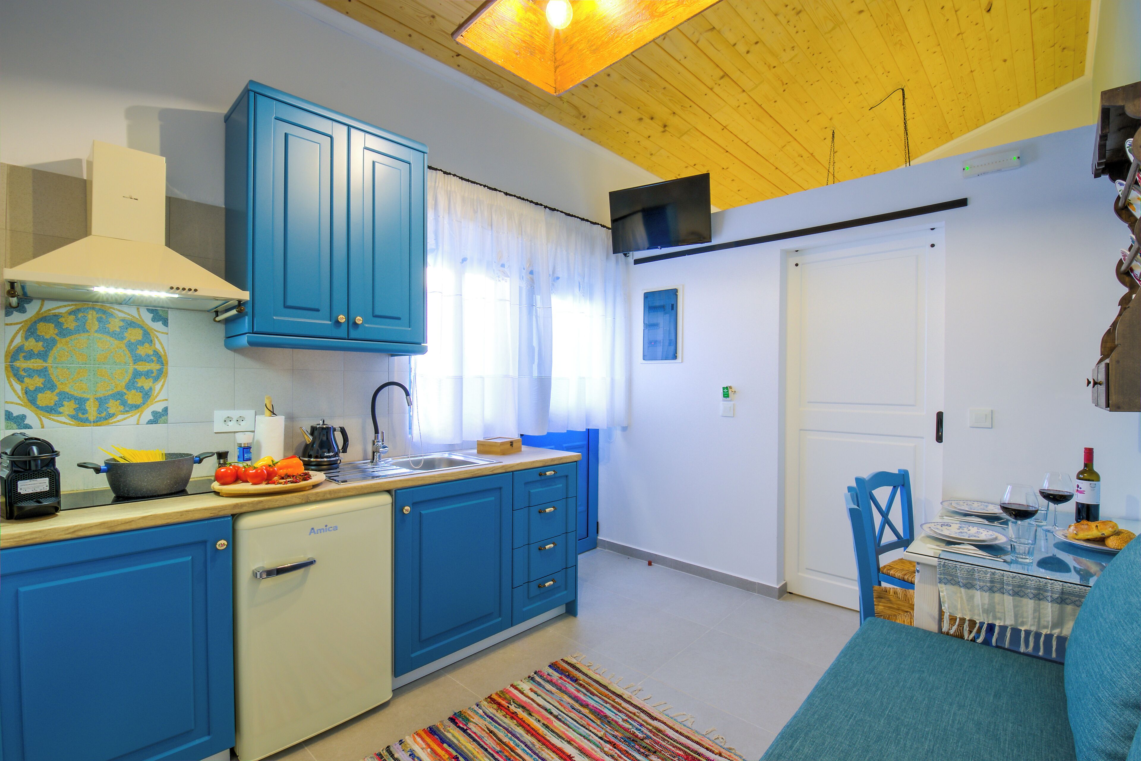A compact kitchen with blue cabinets, a dishwasher, and a dining area with a table set for two.