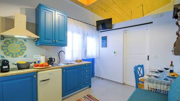A compact kitchen with blue cabinets, a dishwasher, and a dining area with a table set for two.