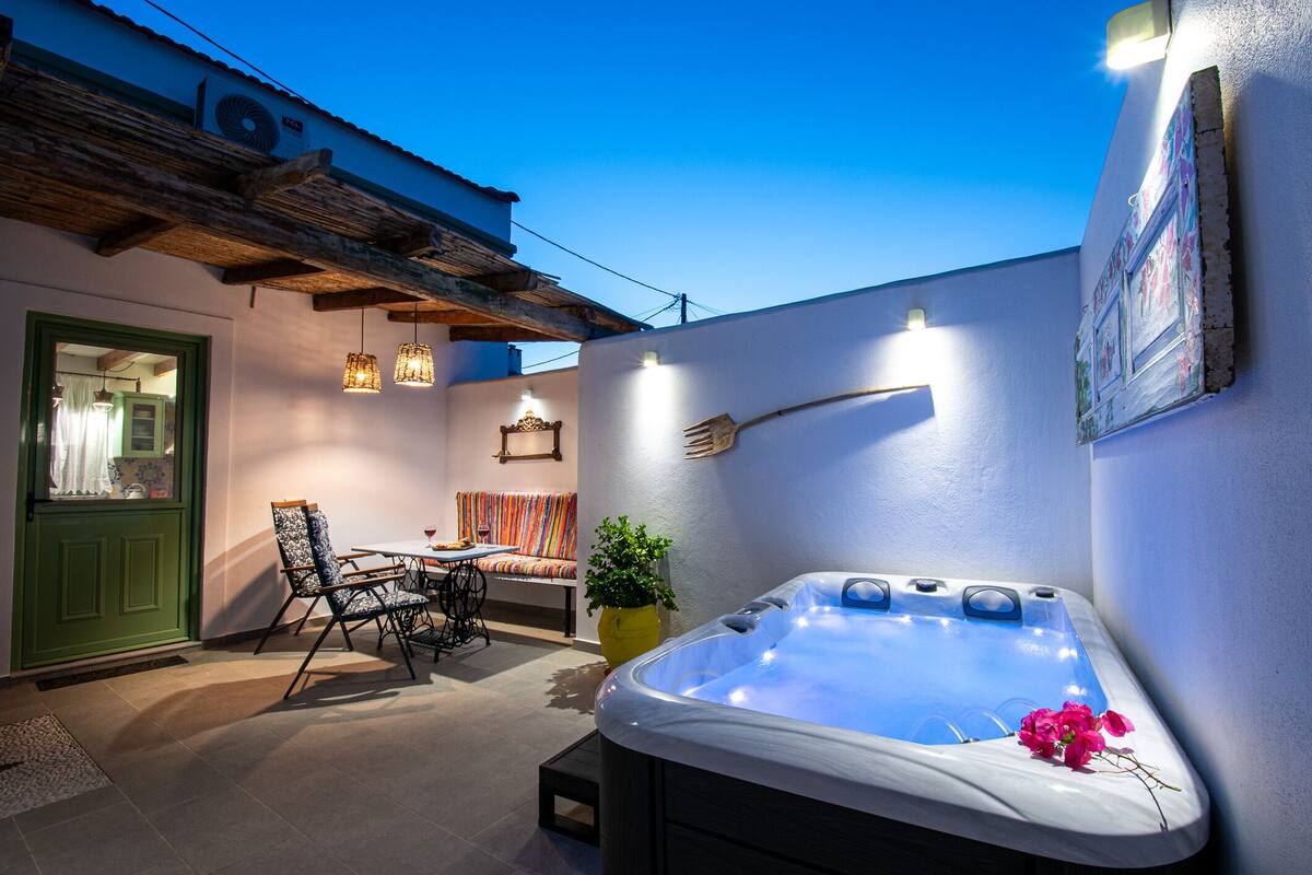 Un patio exterior acogedor con un jacuzzi, una mesa de comedor, sillas y una puerta verde.