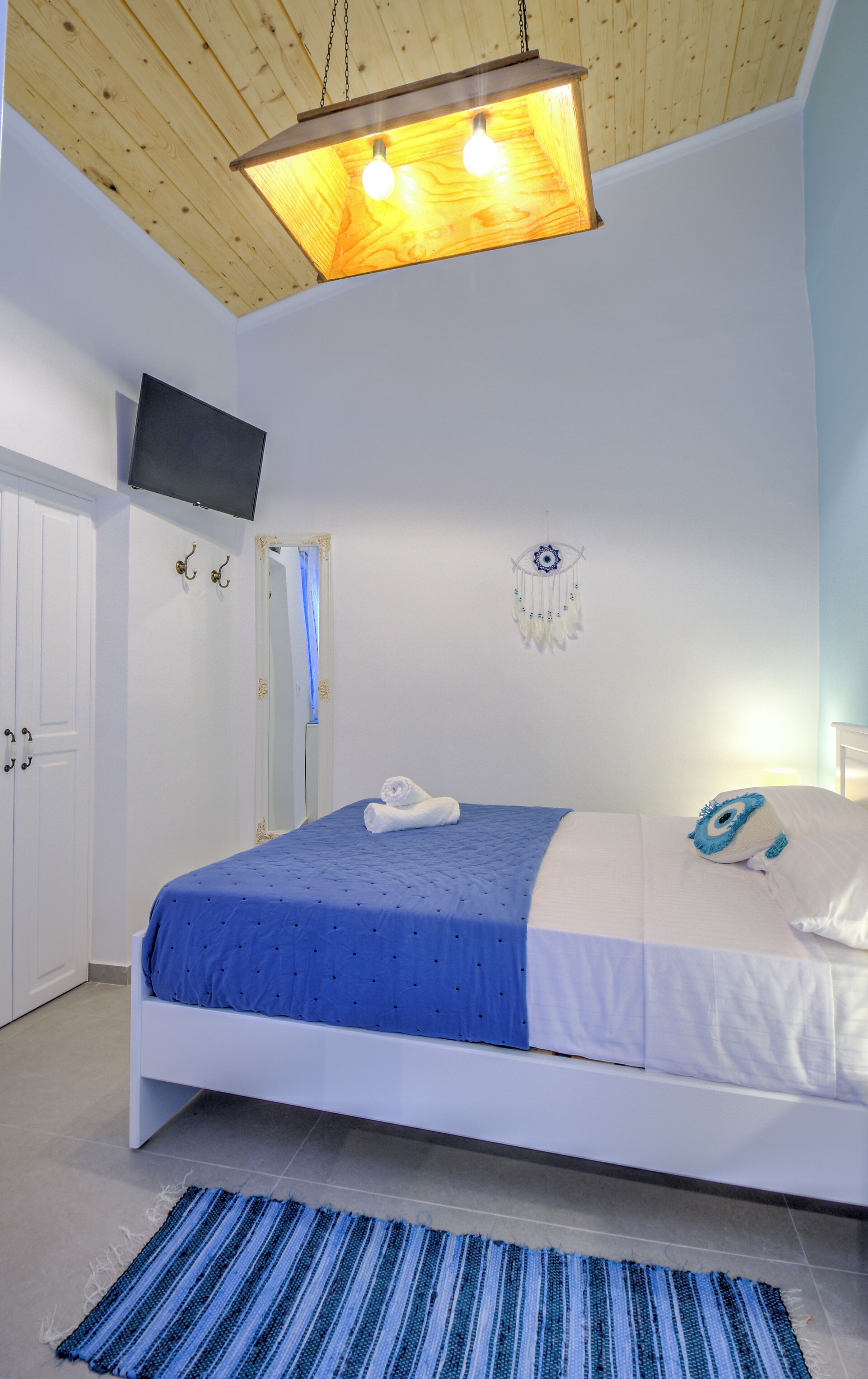 Un dormitorio con cama, televisor montado en la pared y lámpara del techo.