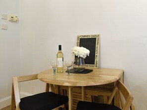 A wooden dining table with two chairs, a bottle of wine, two glasses, and a vase with white flowers.