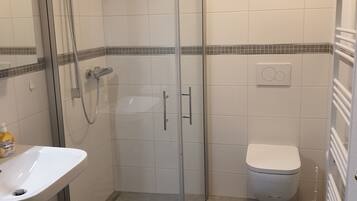 A bathroom with a glass shower enclosure, a white sink, a toilet, and a blue rug on the floor.