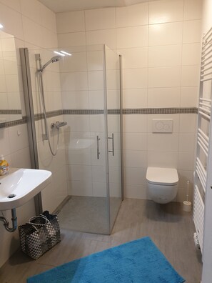 A bathroom with a glass shower enclosure, a white sink, a toilet, and a blue rug on the floor.