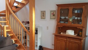Una sala de estar con una escalera de madera, un sofá gris, un aparador de madera con puertas de cristal y una alfombra pequeña.