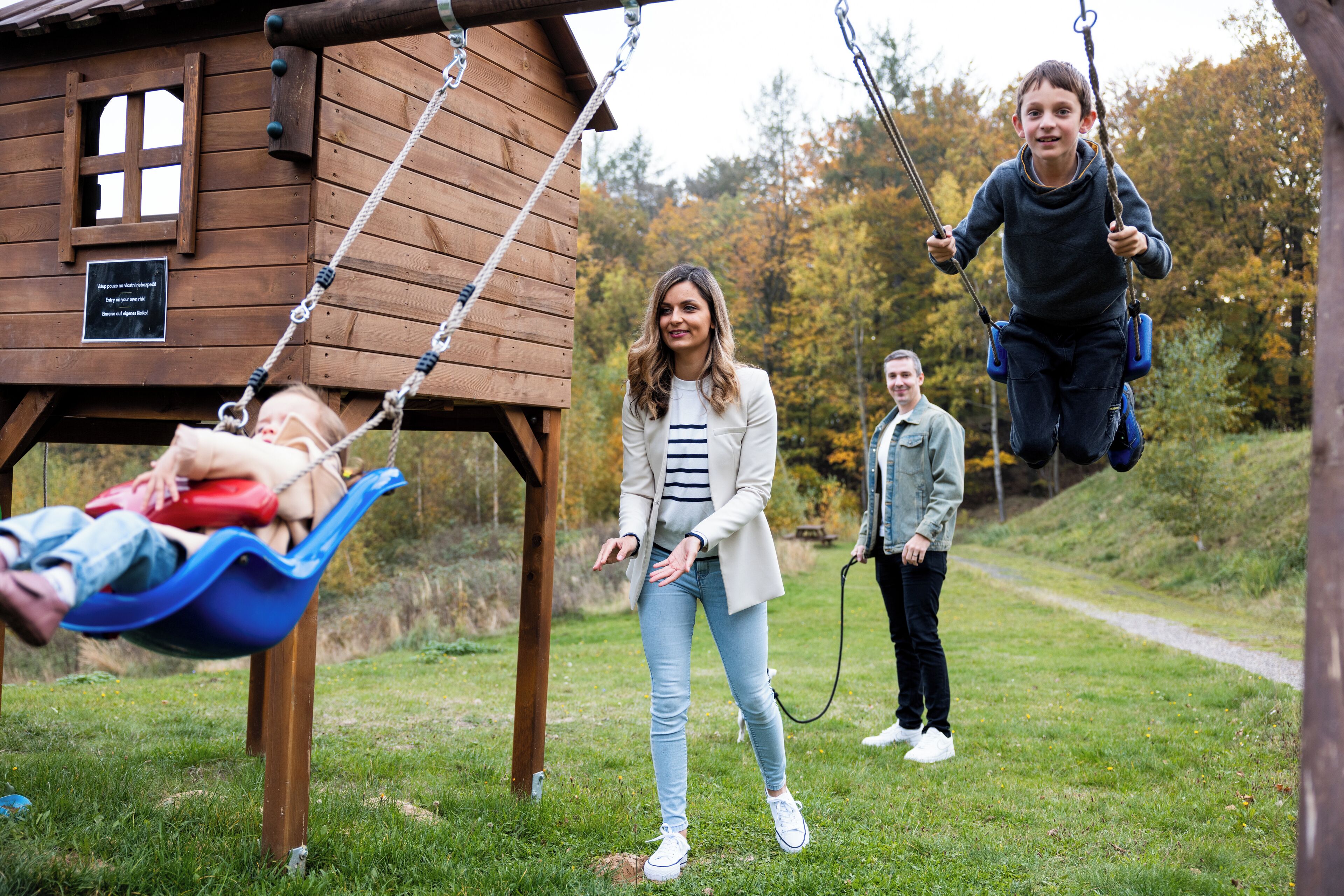 A wooden cabin with a swing set in a grassy area.