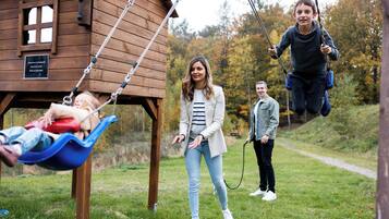 A wooden cabin with a swing set in a grassy area.
