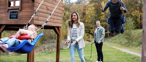 A wooden cabin with a swing set in a grassy area.