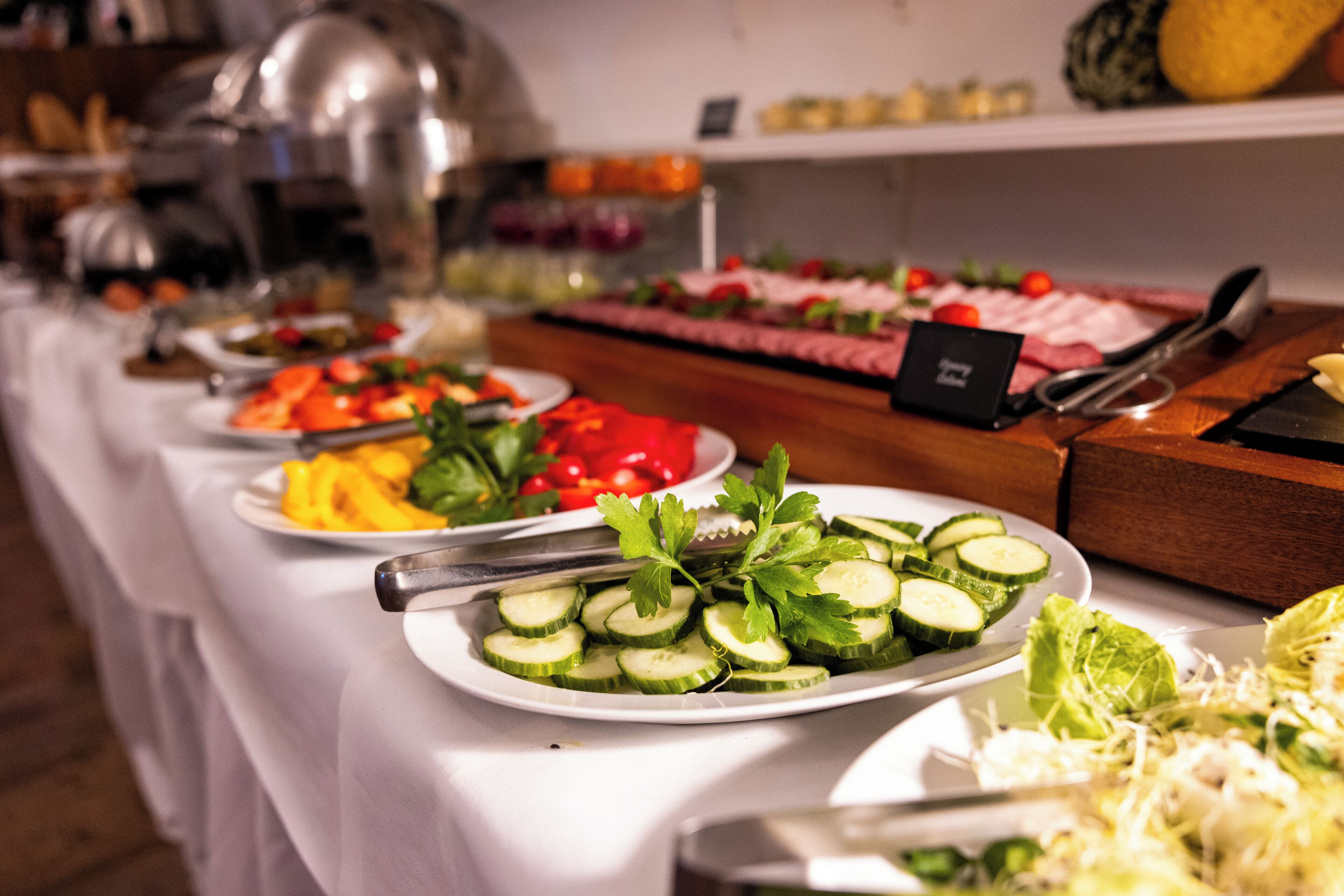 A buffet with various food items including sliced cucumbers, tomatoes, and cheese.