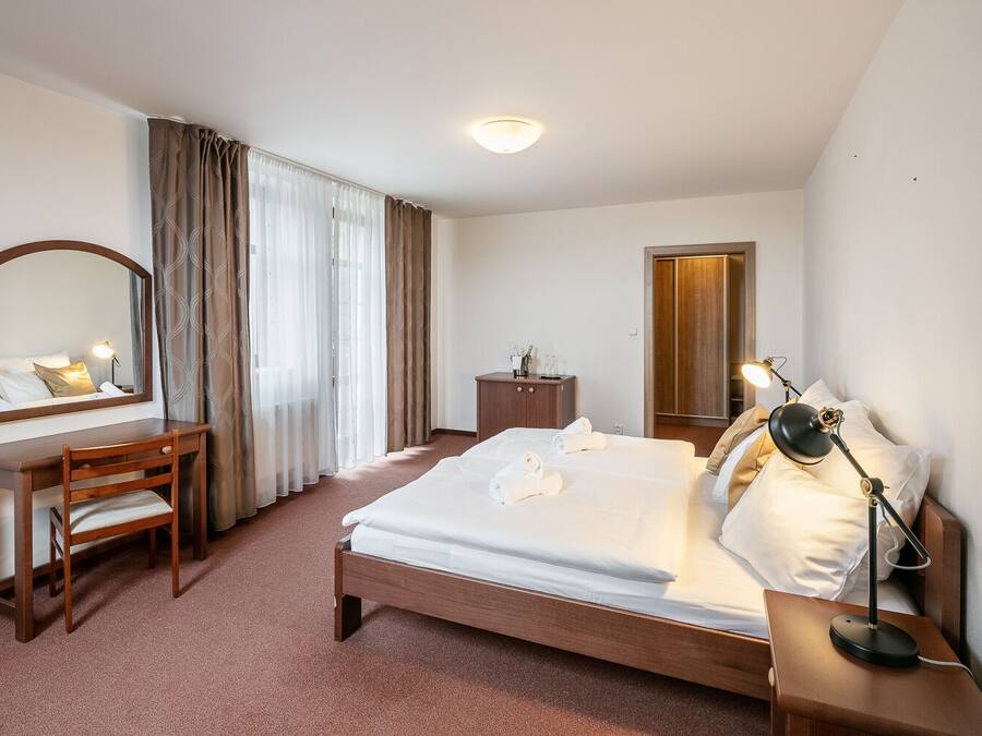 Habitación de hotel con cama, escritorio, silla, cómoda, espejo y mesita de noche con lámpara.