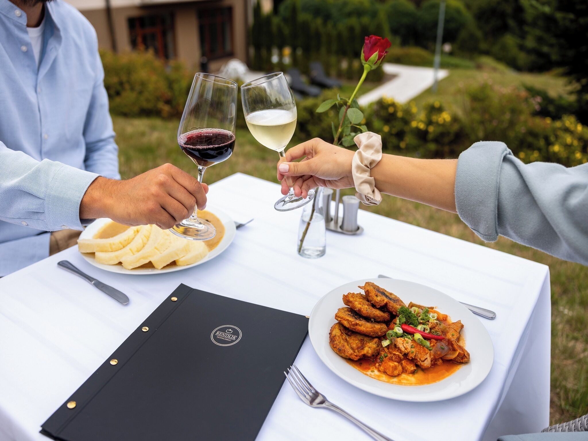 Una mesa de comedor con una carpeta negra, un plato de comida y dos copas de vino.