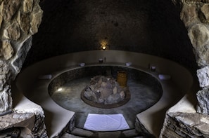 A stone-walled hot tub with a central fire feature, surrounded by seating and towels.