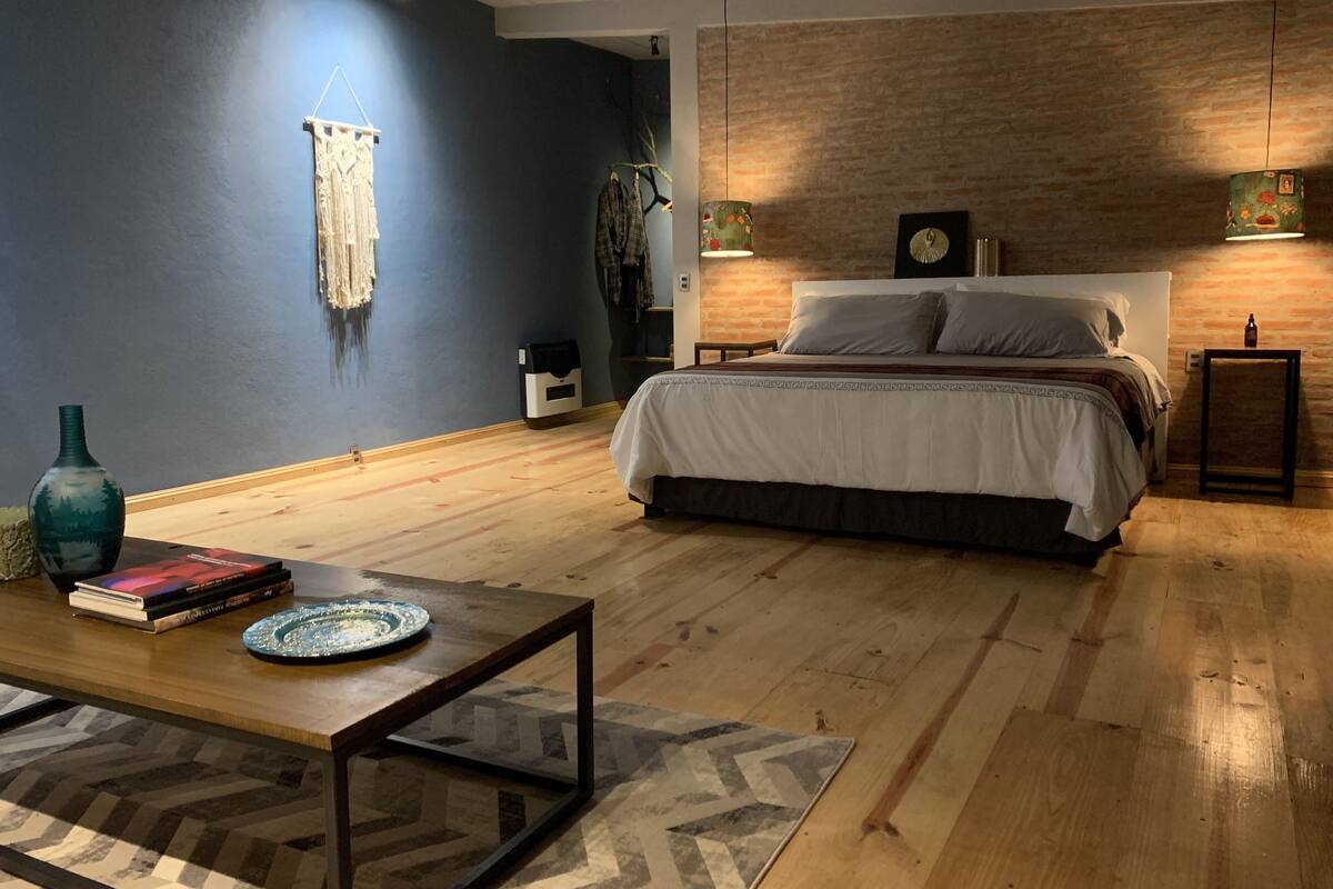 A bedroom with a bed, a wooden floor, a nightstand, a lamp, and a wall-mounted clock.