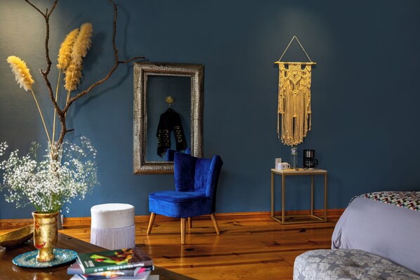 A room with a blue wall, a framed mirror, a blue chair, a small table with a coffee maker, and a hanging macrame piece. - Casa Maria Campiña (Jilotepec)