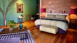 Une chambre à coucher moderne avec un grand lit, un plancher en bois, un mur vert et un mur en briques apparentes.