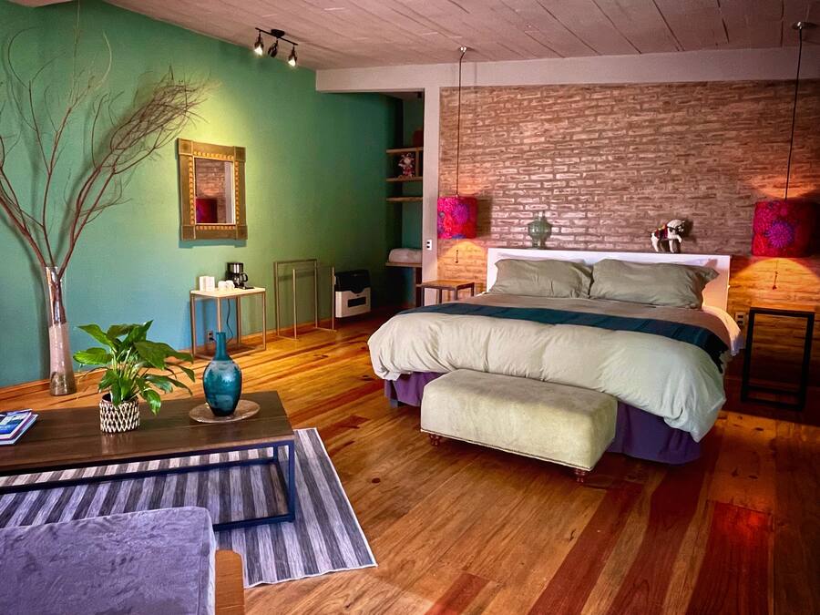 A modern bedroom with a large bed, a wooden floor, a green wall, and a brick accent wall.