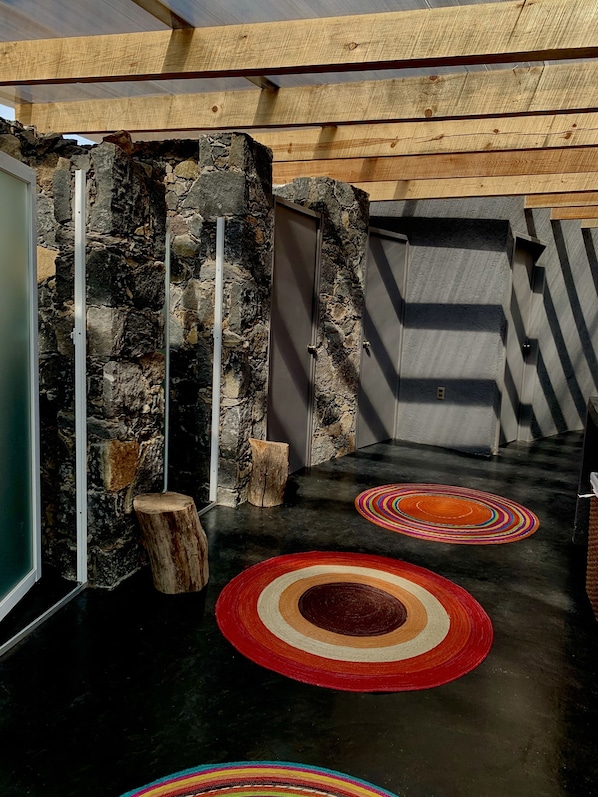 A stone wall with a wooden door, a concrete wall, and a black floor with colorful circular rugs. - Casa Maria Campiña (Jilotepec)