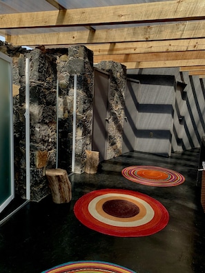 A stone wall with a wooden door, a concrete wall, and a black floor with colorful circular rugs. - Casa Maria Campiña (Jilotepec)