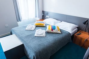 A neatly made bed with a grey blanket, colorful pillows, and folded white towels.