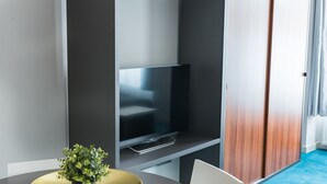 A modern room with a flat-screen TV on a wall, a small potted plant on a round table, and a blue carpeted floor. - Cilindar apartments (Zagreb)