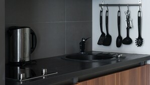 A modern kitchen with wooden cabinets, a black countertop, and a hanging utensil rack. - Cilindar apartments (Zagreb)