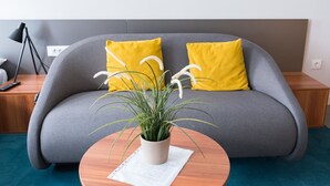 A modern living room with a grey sofa, two yellow pillows, a potted plant, and a wooden side table. - Cilindar apartments (Zagreb)