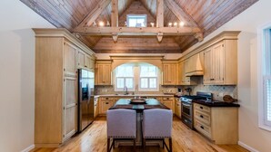 Une cuisine spacieuse avec des meubles en bois, un îlot central doté de tabourets, une grande fenêtre et un plafond voûté.