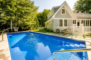 Une piscine avec un panier de basketball, entourée d’une clôture blanche et d’arbres.