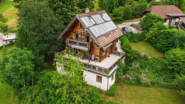 A two-story wooden house with a balcony, surrounded by lush greenery. - Beautiful wooden log house with a first-class view of the mountains! (Bad Goisern am Hallstättersee)