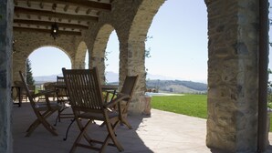 A stone archway patio with wooden chairs and a table, overlooking a green landscape. - Luxury Villa with private pool and Estate Winery in Umbria (Orvieto)