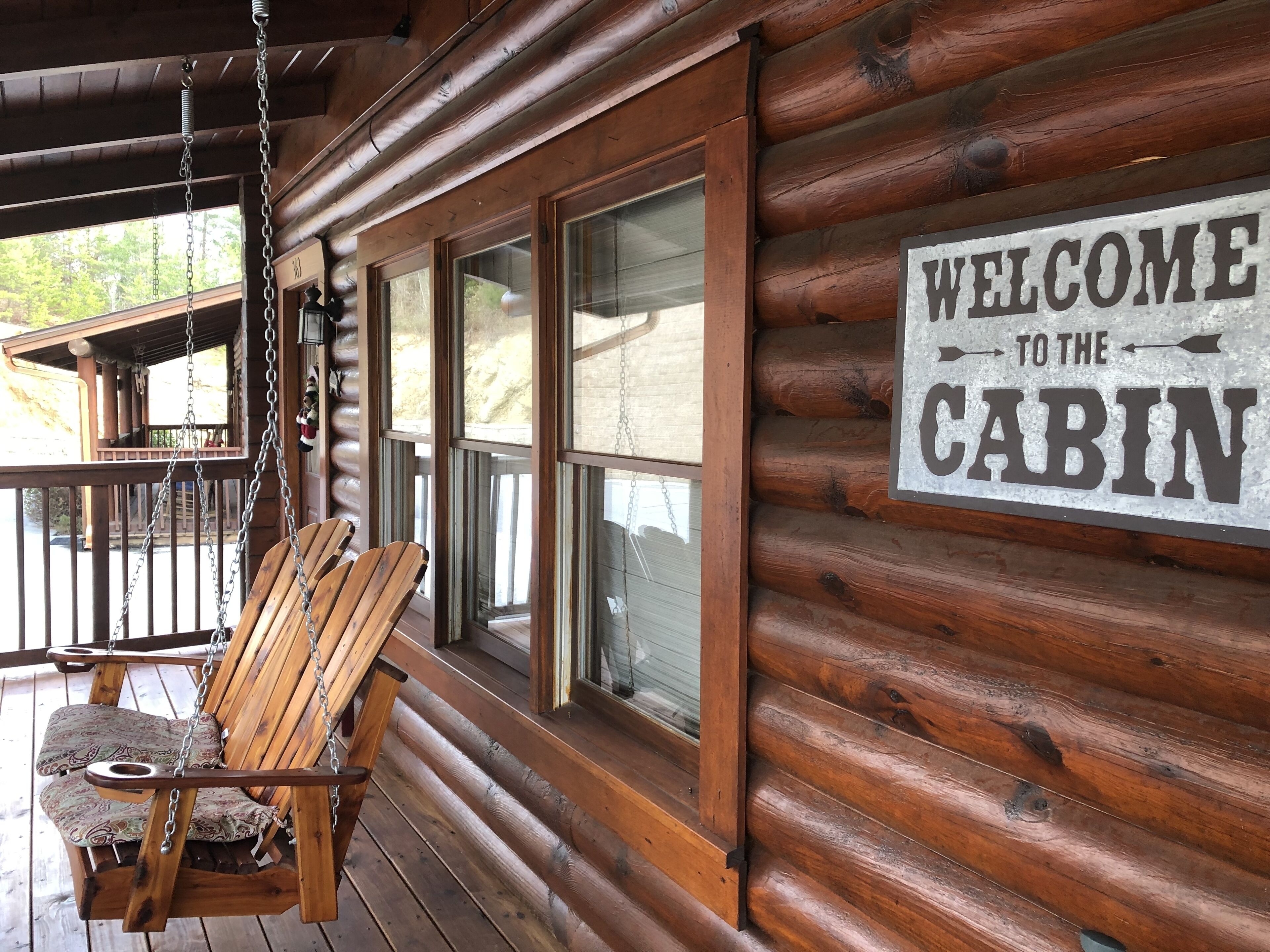 Une cabane en bois avec une chaise suspendue et une pancarte indiquant « Bienvenue à la cabane ».
