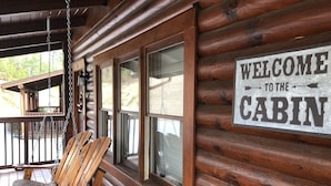 A wooden cabin with a swing chair and a 'Welcome to the Cabin' sign.