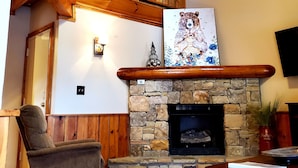 A living room with a stone fireplace, wooden ceiling, and a wooden staircase.