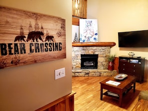 A cozy living room with a stone fireplace, a bear crossing sign, and a television mounted on the wall.